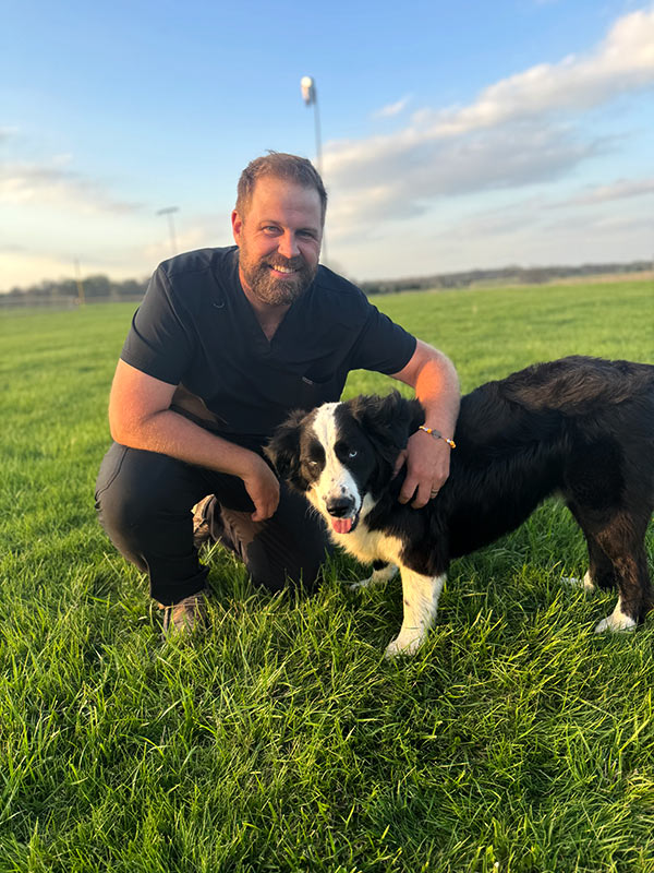 Dr. Aaron Poulignot with a black and white dog outdoors